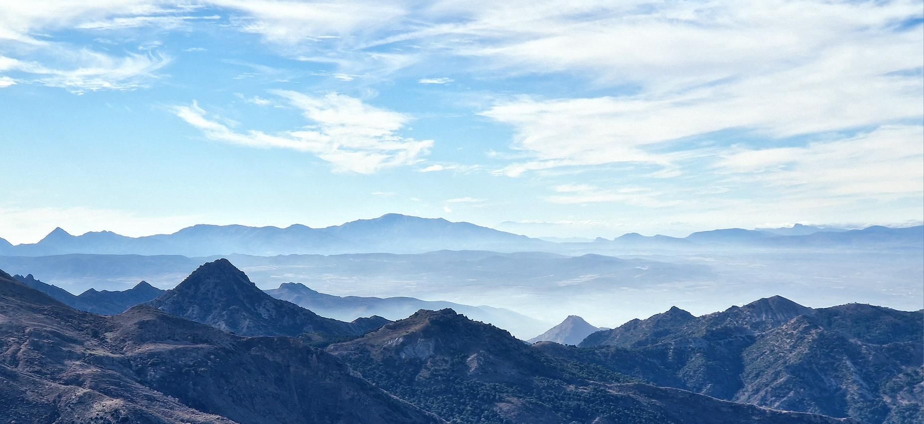 Layered mountain ridges fading into a hazy valley under a blue sky