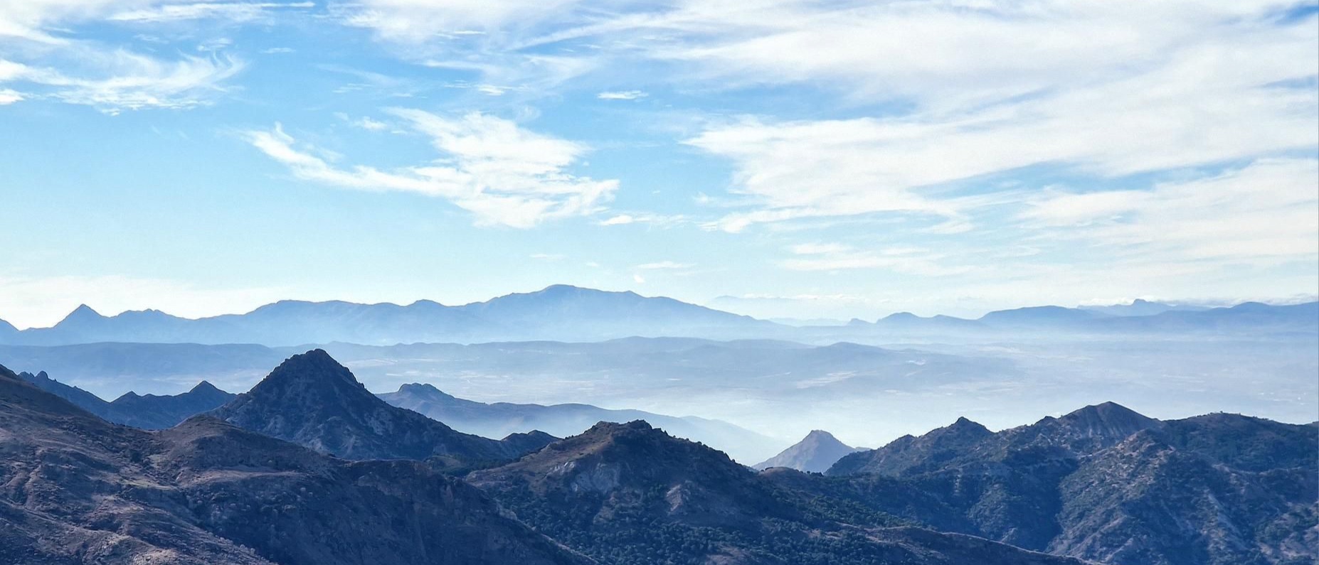 Layered mountain ridges fading into a hazy valley under a blue sky