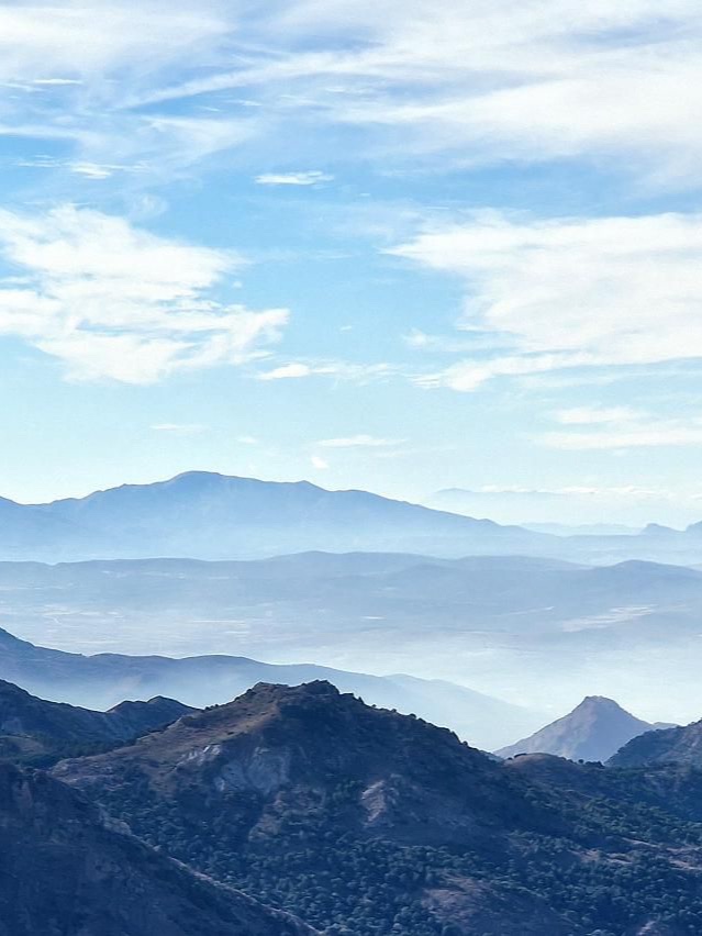 Layered mountain ridges fading into a hazy valley under a blue sky