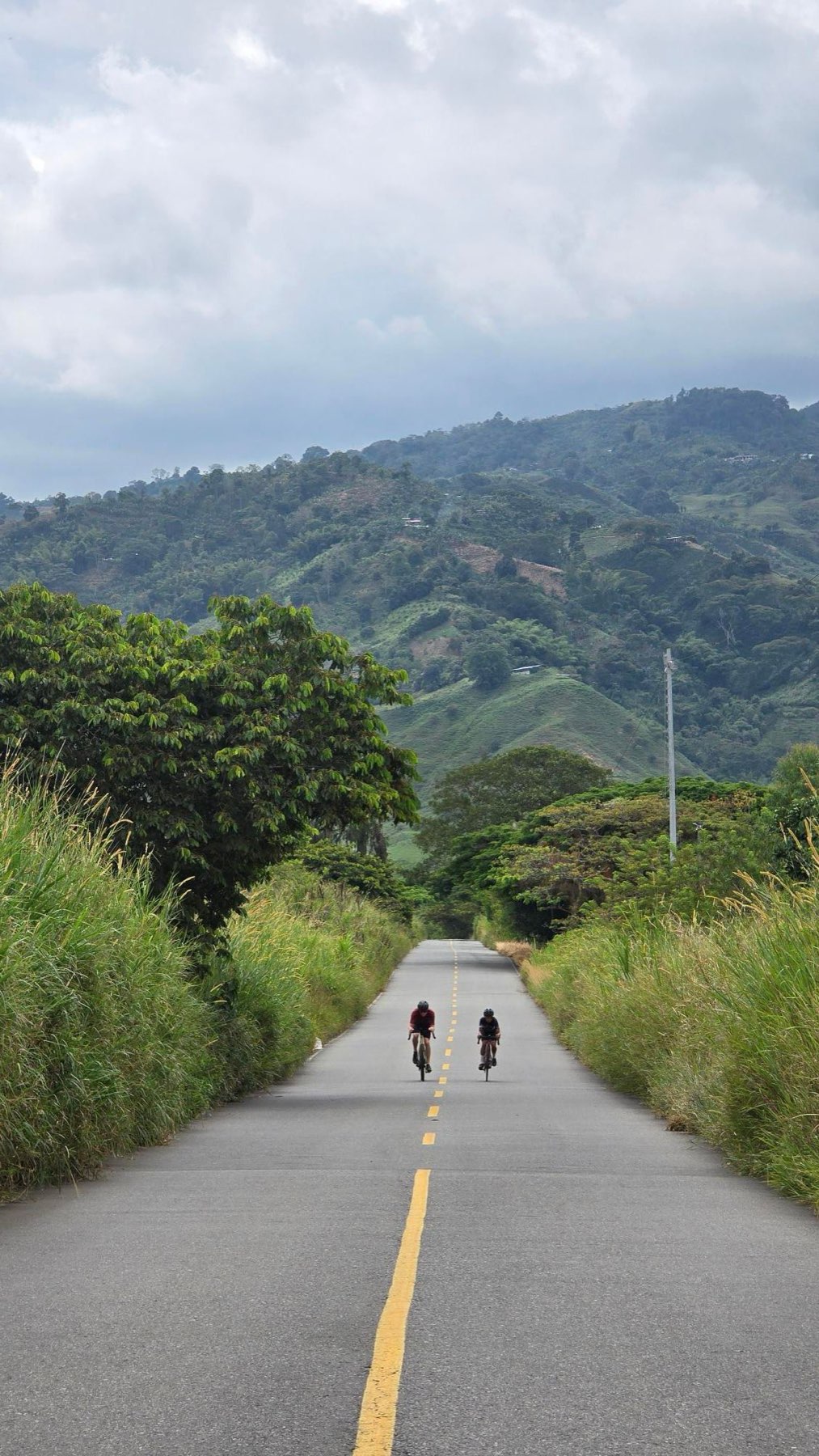 Two cyclists riding side by side up an empty road between green hills